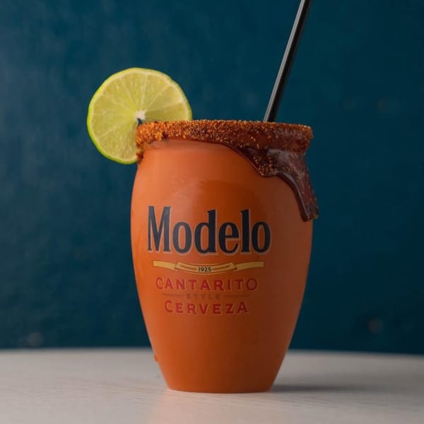 Modelo Cantarito Style Cerveza in an orange mug, garnished with a lime and chili-lime rim.
