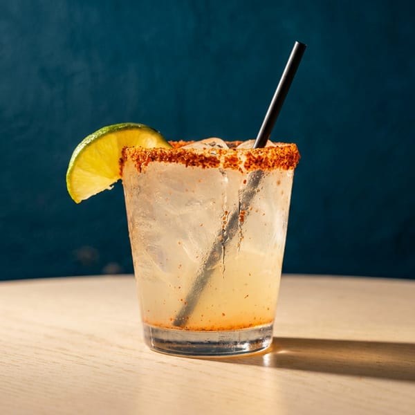 A margarita with a chili-salt rim, lime wedge, and black straw on a wooden table.