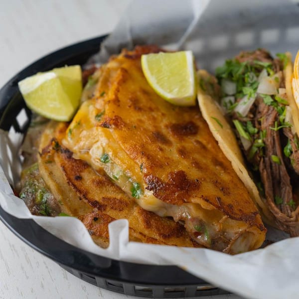 Crispy birria tacos with melted cheese and lime wedges, alongside a traditional beef taco.