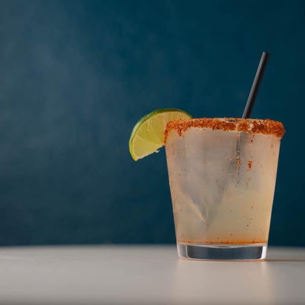 A margarita with a chili-salt rim, lime wedge, and black straw against a blue background.