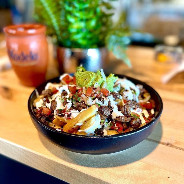 Carne asada fries topped with guacamole, pico de gallo, and sour cream, next to a Modelo cup.