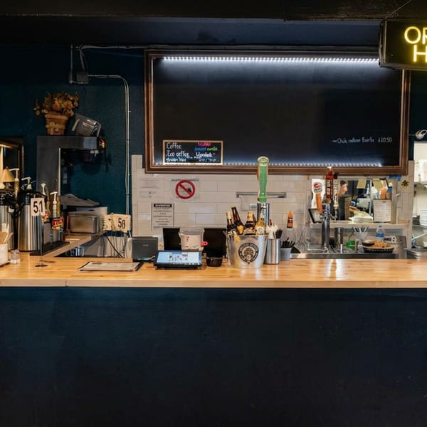 A coffee shop counter with an "ORDER HERE" sign, coffee machines, and a chalkboard menu.